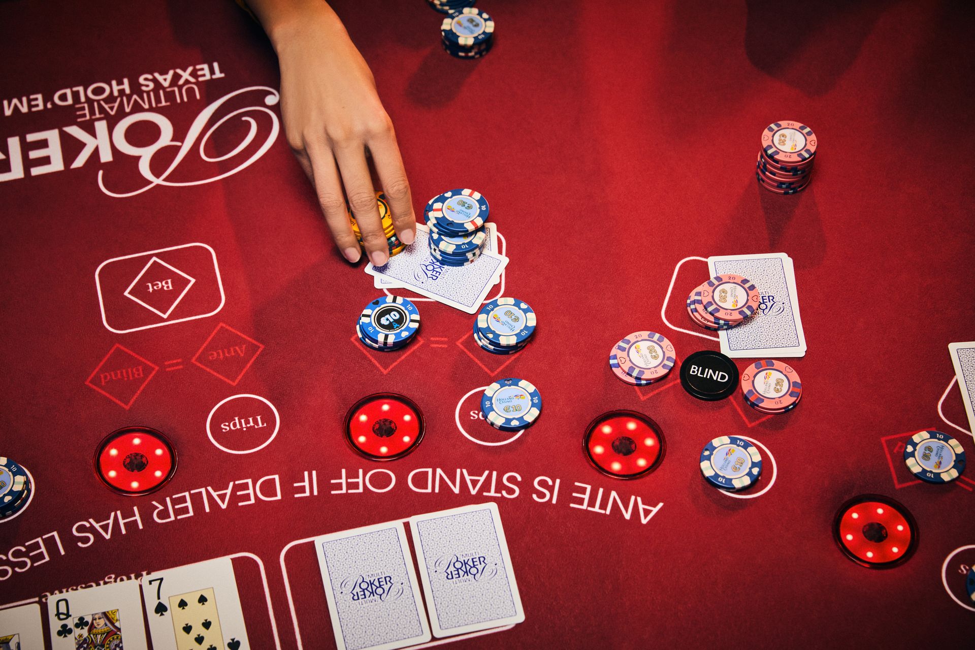 holland-casino-poker-ultimate-texas-hold'em-poker-tafel-met-vrouwelijke-hand-die-waarde-fiches-inzet-op-stapel-kaarten-legt
