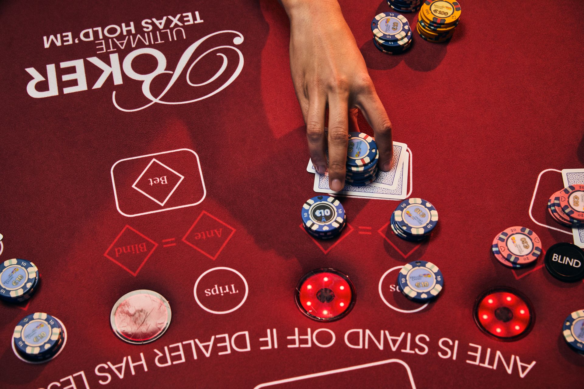 holland-casino-poker-ultimate-texas-hold'em-poker-tafel-met-vrouwelijke-hand-die-waarde-fiches-inzet-op-stapel-kaarten-legt