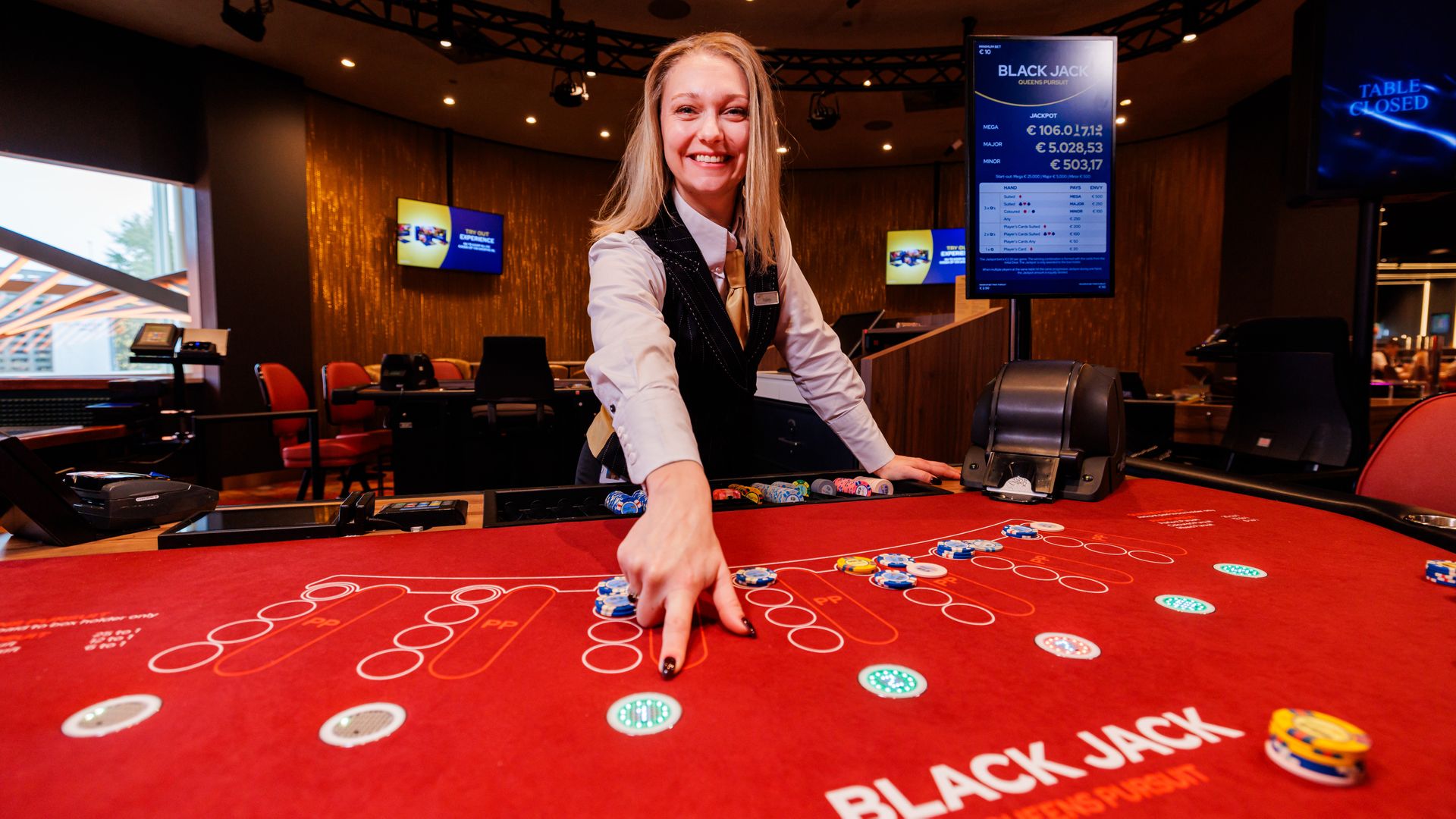 De dealer wijst op de coinspot van de Black Jack "Queens Pursuit" speeltafel